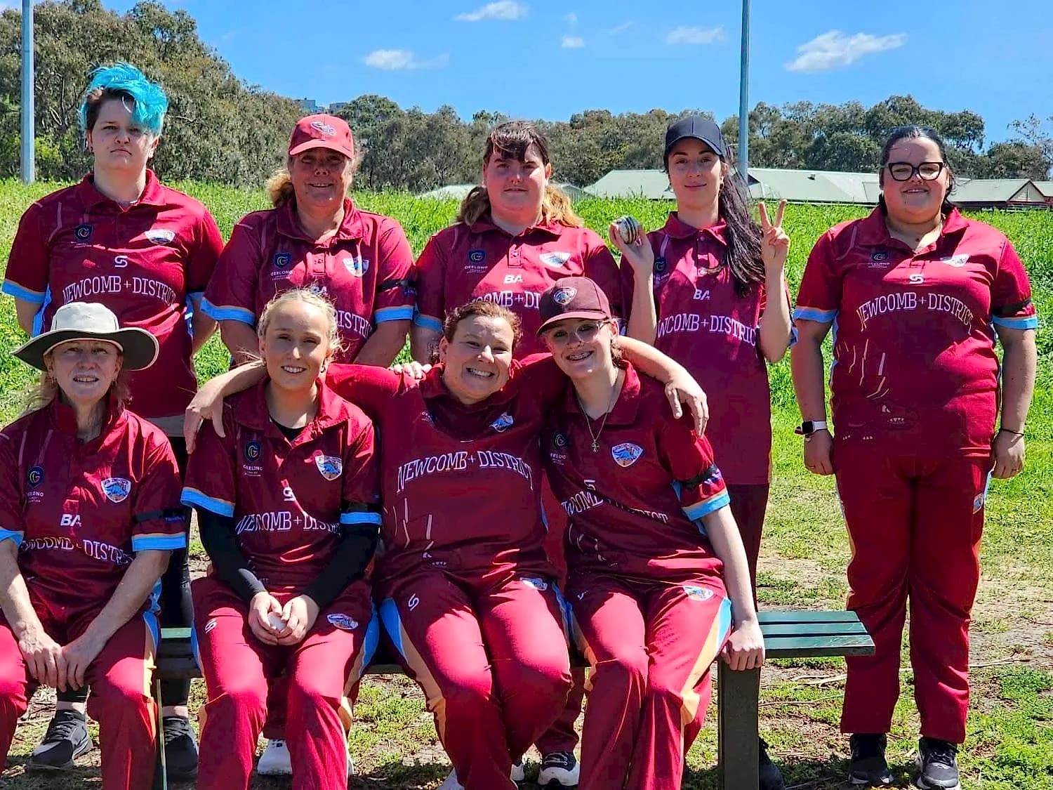 Newcomb & District women's team gathered around a park bench on a sunny day